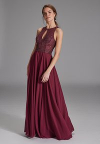 Robe bordeaux avec un corsage en perles, décolleté en trou de serrure, design sans manches et jupe fluide, fabriquée à partir d'un tissu léger.