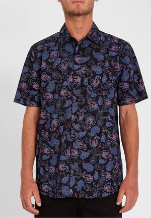 Mann trägt ein schwarzes, kurzärmliges Hemd mit Knöpfen, verziert mit abstrakten blauen und violetten Blumen- und Wirbelmustern.