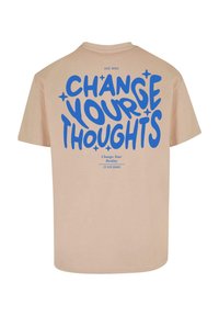 Beige bomulds t-shirt med blå grafisk tekst på ryggen: "ÆNDRE DINE TANKER" med yderligere tekst nedenfor, afslappet pasform, korte ærmer.
