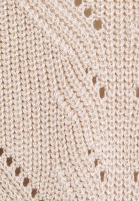 Tissu tricoté en écru avec un motif texturé. Il présente des points en relief et des trous ajourés créant un design délicat.