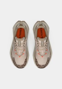 Chaussures de sport beige avec des accents marron texturés, des touches orange et un design structuré. Elles comportent des lacets et une semelle rembourrée.