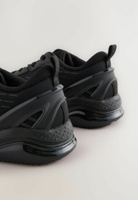 Schwarze Sportschuhe haben ein strukturiertes Mesh-Obermaterial, eine gepolsterte Sohle, ein schlankes Design mit glänzenden Akzenten und einen gepolsterten Schaft.