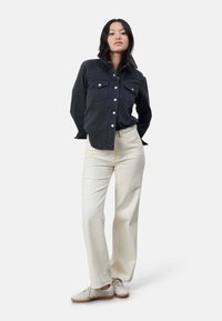 Donkerdenimshirt met knoopsluiting en twee borstzakken, gecombineerd met lichtgeribbelde wijde broek en grijze sneakers.