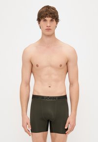 Õlivärvi boxer-püksikud musta brändiga vöörihmaga. Sile kangas, istuv disain, ees olev tasku ja lühike jooksupikkus.