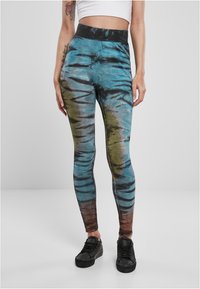 Flerfärgade leggings i blå, grön och brun tie-dye mönster. Hög midja, elastiskt tyg, figurnära design, bärs med svarta sneakers.