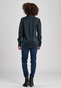 Mörkgrön skjorta med knappar, rundad nederkant, långa ärmar och manschetter, tillsammans med blå jeans och svarta ankle boots.