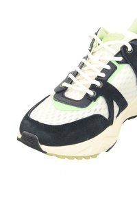 Athletic-Sneaker aus weißem Mesh mit schwarzen Wildleder-Überzügen, hellgrünen Akzenten, weißen Schnürsenkeln und einer dicken beigen Sohle.