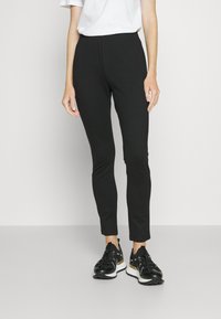 Sorte, tettsittende bukser laget av et glatt stoff med elastisk midje, som smalner inn mot ankelen. Brukt med svarte treningssko.