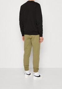Felpa nera con collo rotondo, abbinata a pantaloni jogger verde oliva. L'outfit è completato da sneakers bianche con dettagli neri.