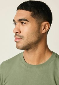 Olivovo zelené bavlnené tričko s okrúhlym výstrihom, krátkymi rukávmi a čistými švami. Hladká textúra so priliehavým strihom.