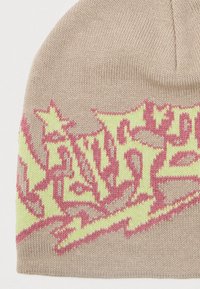 Beżowa dziana czapka z żółtym i różowym abstrakcyjnym wzorem przypominającym płomienie na środkowej części.