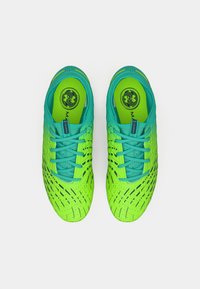 Bright green and teal soccer cleats with laces, black geometric patterns, and branded insoles placed side by side on a white background.