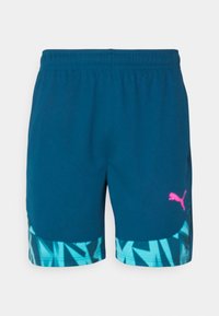 Blaue Sportshorts mit einem elastischen Bund. Sie haben ein geometrisches türkisfarbenes Muster am Saum und ein pinkes Puma-Logo auf der Vorderseite.