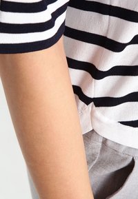 Top a maniche corte a righe blu navy e bianche in tessuto a maglia, con vestibilità casual e dettaglio a contrasto sull'orlo. Tessuto grigio visibile sotto.