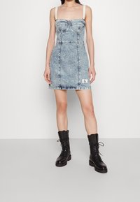 Denim minikjol i ljusblått med strukturerad byst, justerbara axelband och en synlig logotypapplikation. Kombinerad med svarta snörade kängor.