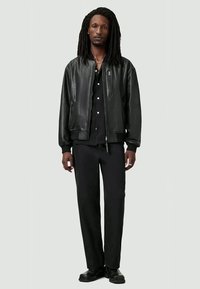 Black leather bomber jacket, ribbed cuffs, and hem, paired with a dark button-up shirt and black trousers, completing a monochromatic look.