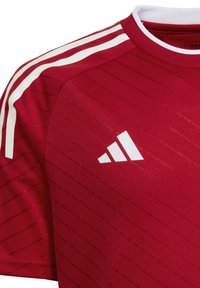 Maglietta sportiva rossa con righe orizzontali, dettagli bianchi sulle maniche e logo Adidas bianco sul petto. Finitura in tessuto testurizzato.