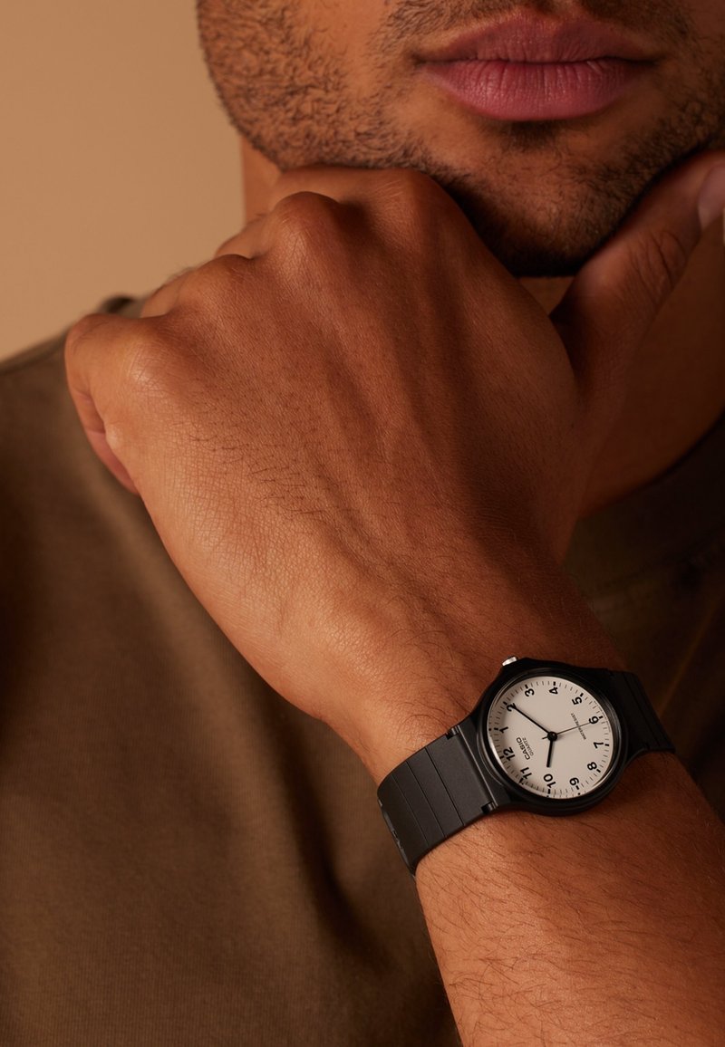 Gros plan sur le poignet d'une personne portant une montre analogique noire avec un cadran blanc, des chiffres noirs et trois aiguilles indiquant l'heure.