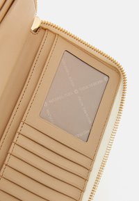 Beige zip-around wallet with multiple card slots and a clear ID window featuring fabric branded with diagonal "Michael Kors" text.