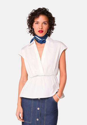 Witte korte mouwen blouse met een diepe V-hals, ingezette taille en decoratieve stiksels. Draagt met een blauwe sjaal en denimrok.