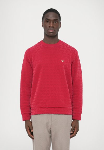 Red, quilted sweatshirt with a round neckline and long sleeves. Features a small gold logo on the chest. Textured fabric with geometric pattern.