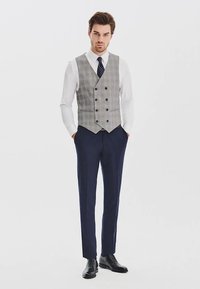 Męski strój formalny składający się z jasnoszarej w kratę kamizelki, białej koszuli, granatowych spodni i czarnych butów. Kamizelka zapinana na podwójne guziki.