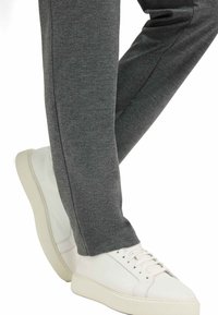 Joggers gris foncé texturés avec une coupe slim, associés à des baskets blanches en cuir ayant un motif de semelle subtil et des lacets ton sur ton.