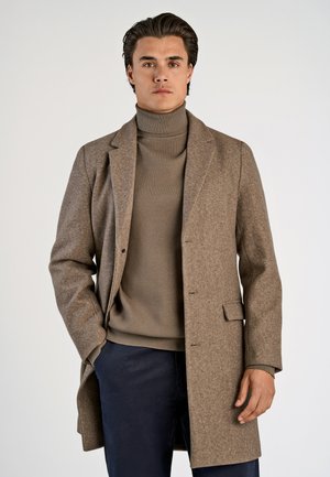 Brown wool overcoat with a notched collar, single-breasted design, and side pockets. Worn over a light brown turtleneck sweater.