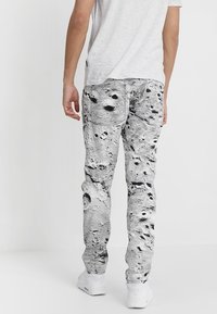 Grå byxor med ett månkratertryck, slim fit och subtil textur. Bakfickor synliga, kompletterat med vita sneakers.