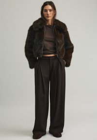 Giacca bomber in pelliccia sintetica marrone con collo alto, abbinata a un top corto marrone e pantaloni a gamba larga. Tessuto morbido e vestibilità rilassata.