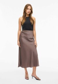 Sort ærmeløs top, brun satin midi-nederdel, glat tekstur, flydende form, parret med sorte højhælede sandaler med guldaccenter.