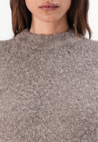 Pull en maille brun clair avec un col haut, en tissu en laine doux et texturé, et une coupe légèrement ample.