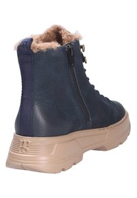 Botte d'hiver en cuir bleu marine avec semelle en caoutchouc beige, fermeture éclair latérale, lacets à l'avant, boucle en tissu bleu marine au talon, et doublure en fausse fourrure beige.