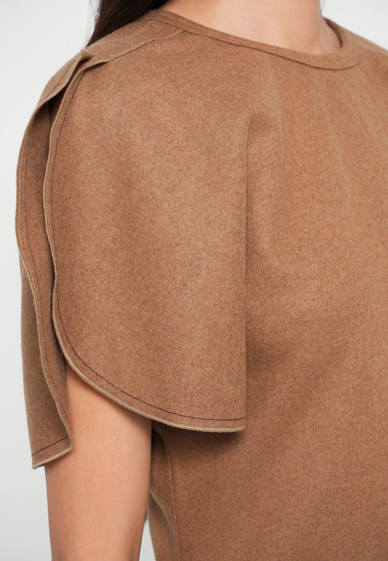 Top in lana marrone con scollatura rotonda, maniche corte caratterizzate da un design piegato unico e cuciture in vista lungo i bordi.
