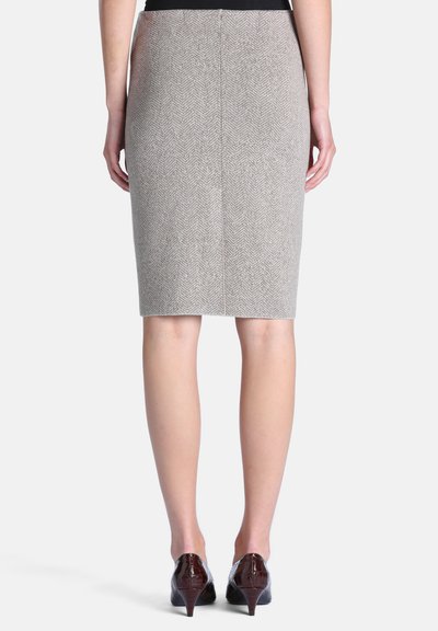 Femme portant une jupe crayon chevron grise longueur genou et des chaussures à talons hauts marron foncé, debout les mains détendues le long du corps.