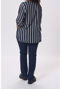 Blouse à rayures bleu marine et blanches avec manches trois-quarts, associée à un jean en denim bleu foncé et des chaussures noires épaisses.