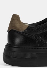 Chaussure en cuir noir avec un accent en daim au talon. Présente une surface texturée et une semelle noire épaisse et à motifs pour une meilleure adhérence et durabilité.