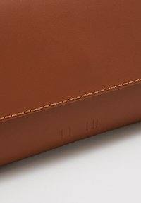 Ruskea nahkainen lompakko, jossa on teksturoitu pinta. Siinä on kontrastoiva vaaleanruskea ommelrivi ja huomaamaton kohokuviointi alaosassa.