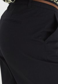 Pantalons noirs avec une texture lisse, dotés d'une poche arrière et d'une passante de ceinture. La vue en gros plan met en évidence la forme et les détails de couture.