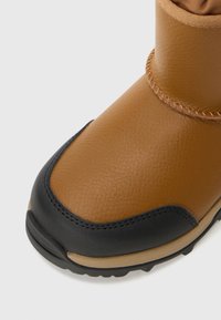 Detaljbild av en brun vattentät boot med en strukturerad yta, svart gummisula och en kontrasterande beige del nära botten.