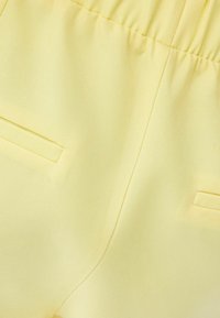 Light yellow fabric featuring a smooth texture, elastic waistband, and two side pockets with a clean, minimal design.