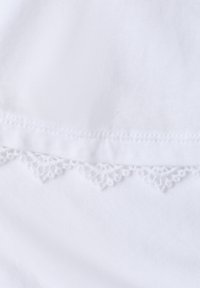 Tissu blanc avec un ourlet présentant une délicate bordure en dentelle triangulaire et des coutures fines le long du bord.