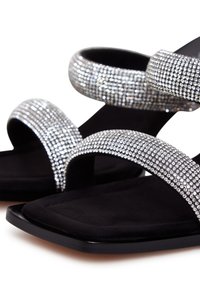 Zwarte platte sandalen met twee brede banden versierd met heldere rhinestones, die een gestructureerd oppervlak en een vierkante te ontwerp benadrukken.