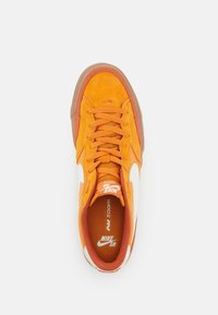 Sneaker in suede arancione con logo bianco; presenta una suola in gomma, punta tonda e design con lacci. L'interno è dotato di soletta con marchio e colletto imbottito.