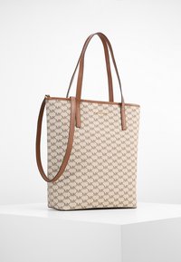 Beige tote-väska med bruna läderremmar, som har ett upprepande MK-logomönster. Väskan har en rektangulär form och en slät textur.