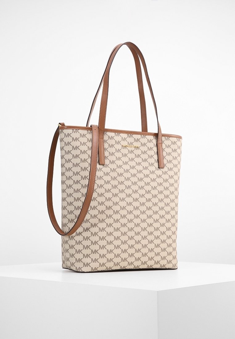 Beige tote-väska med bruna läderremmar, som har ett upprepande MK-logomönster. Väskan har en rektangulär form och en slät textur.