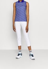 Ärmlös blå polo med vita och lila mönster, matchad med vita knälånga byxor och sportiga skor med svarta, marinblå och aqua detaljer.