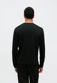 Czarna koszula z długim rękawem wykonana z miękkiego materiału, z okrągłym dekoltem i luźnym krojem. Charakteryzuje się minimalistycznym designem, bez widocznych logo czy wzorów.