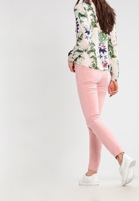 Světle růžové skinny džíny s mírným elastanem, v kombinaci s květinovým vzorem dlouhým rukávem a bílými teniskami s gumovou podrážkou.