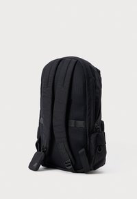 Mochila negra fabricada con material duradero, que cuenta con correas acolchadas, un panel de malla y un bolsillo lateral con un lazo de hardware para accesorios.